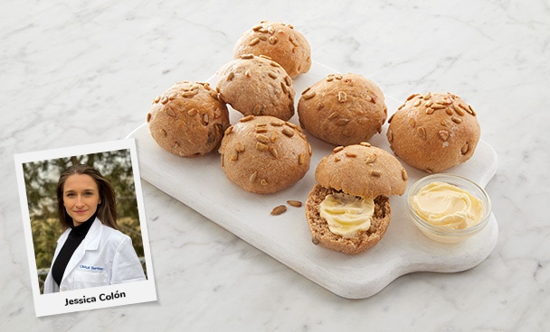 Photo of Jessica Colón, RDN, LD next to seven plated sourdough sunflower seed rolls and a smattering of butter. 
