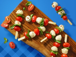 Cherry tomatoes, mozzarella cheese balls, basil and balsamic glaze on skewers. Served alongside plate with a sandwich, potato chips and watermelon slices.