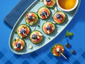 Assembled bites of cucumber, watermelon, blueberry, feta, honey and herbs.