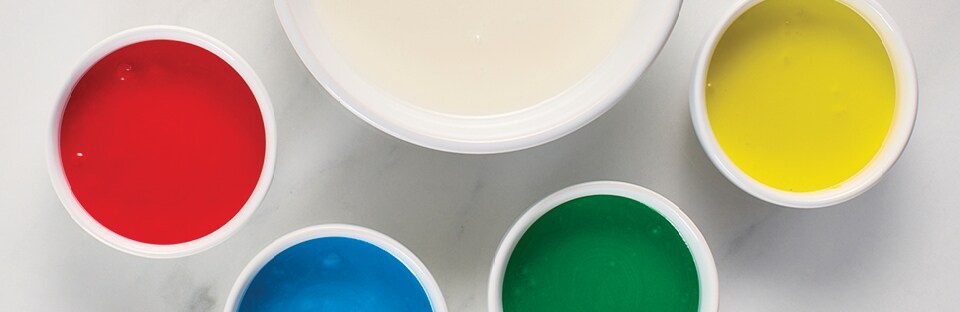 Overhead view of 1 large white bowl of white royal icing surrounded by 4 smaller bowls of royal icing, dyed red, blue, green and yellow.