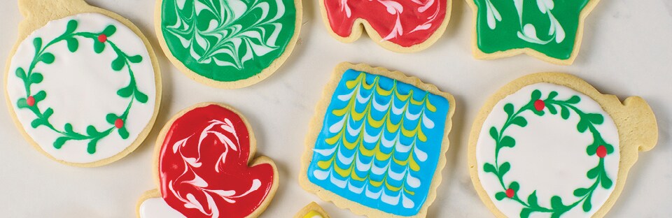 A variety of decorated sugar cookies, using the toothpick icing method, on a white marble surface.
