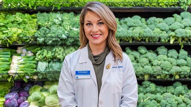 Image of a Registered Dietitian standing in front of shelf of leafy green vegetables