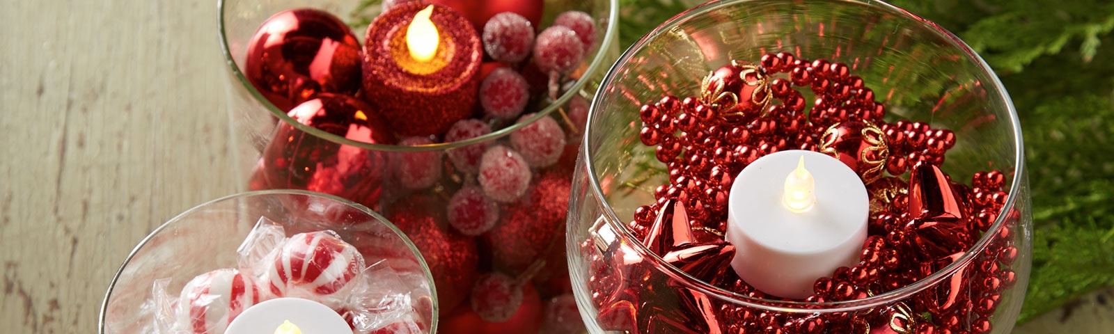 Glass vases filled with red beads, peppermints and cranberries with tea lights placed in the middle