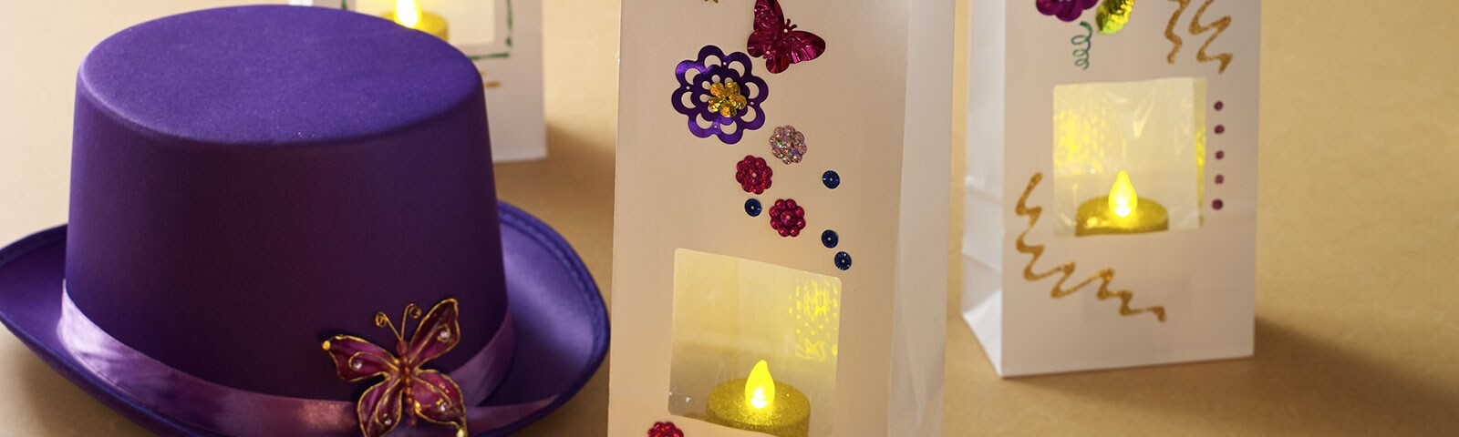 A purple top hat with a decorative brooch along with three white paper bags, decorated and filled with an LED candle A purple top hat with a decorative brooch along with three white paper bags, decorated and filled with an LED candle