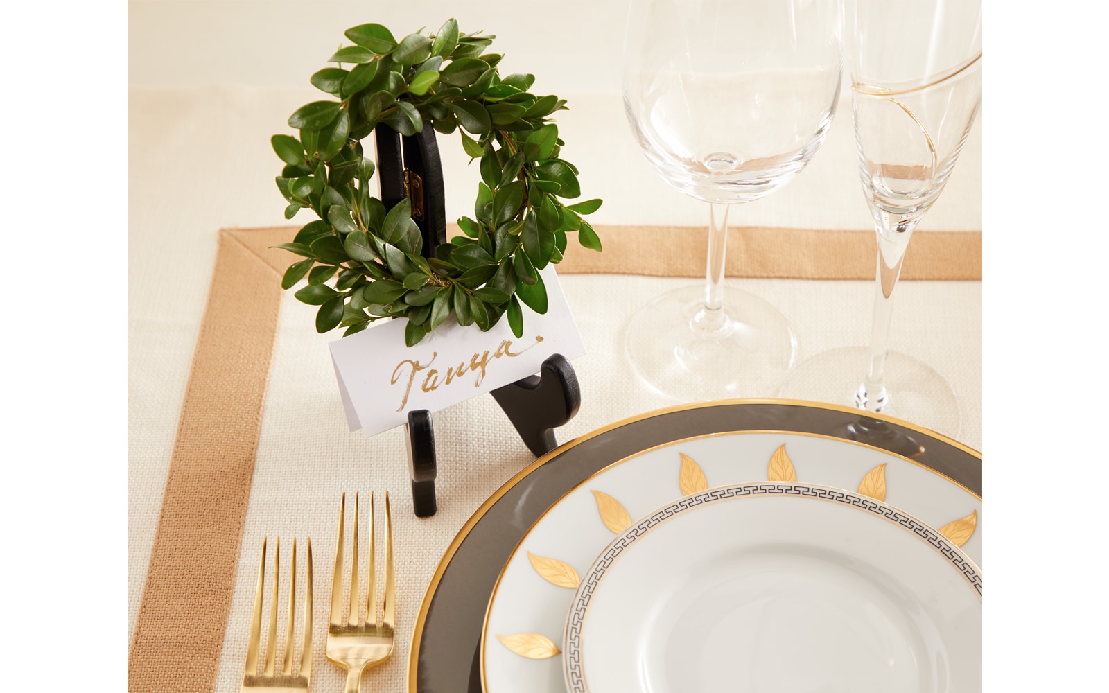 A name card sits in a small picture frame holder with a tiny wreath at the top, beside this is an ornate dinner plate setting A name card sits in a small picture frame holder with a tiny wreath at the top, beside this is an ornate dinner plate setting
