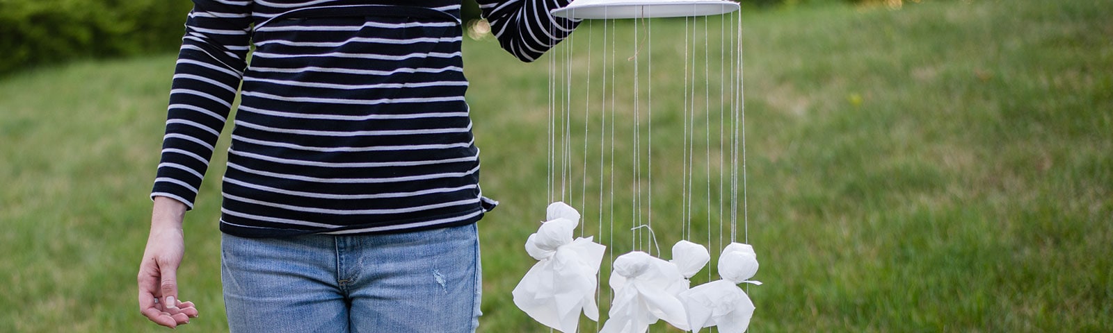 Woman holding a homemade mobile with multiple tissue ghosts hanging from a plate Woman holding a homemade mobile with multiple tissue ghosts hanging from a plate