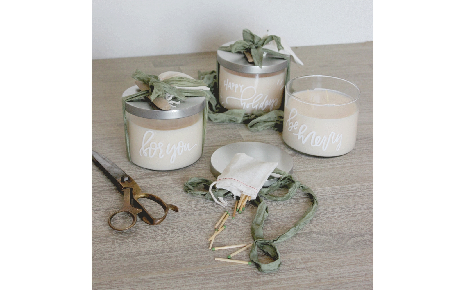 White candles with silver lids and words written on the glass sit on a table next to scissors and matches White candles with silver lids and words written on the glass sit on a table next to scissors and matches