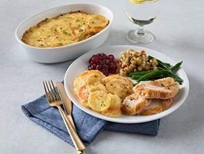 Plated Thanksgiving meal (turkey, green beans, stuffing, cranberry sauce, scalloped potatoes) featuring perfectly baked cheesy scalloped potatoes.