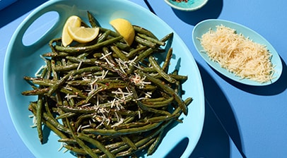 Plated spicy green beans topped with Parmesan cheese. Sides of Parmesan and extra crushed red peppers are included to adjust flavors.